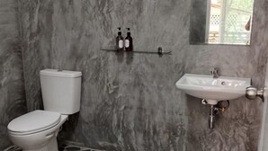 A bathroom with a toilet, a sink, and a shelf with bottles. - Baan Namthip Homestay Trang บ้านน้าทิพย์ โฮมสเตย์ตรัง (Sikao)
