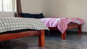 Deux lits en bois avec des draps différents, une fenêtre avec des rideaux et un sol carrelé.