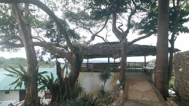 A covered outdoor seating area with a stone pathway leading to it, surrounded by trees and plants. - RedDoorz @ Garvs Boutique Hotel Boracay (Boracay Island)