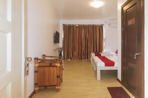 Une chambre d’hôtel avec un lit en bois, une petite table, une chaise, un téléviseur et un rideau.