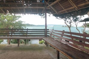 A wooden bench under a thatched roof overlooking a body of water.