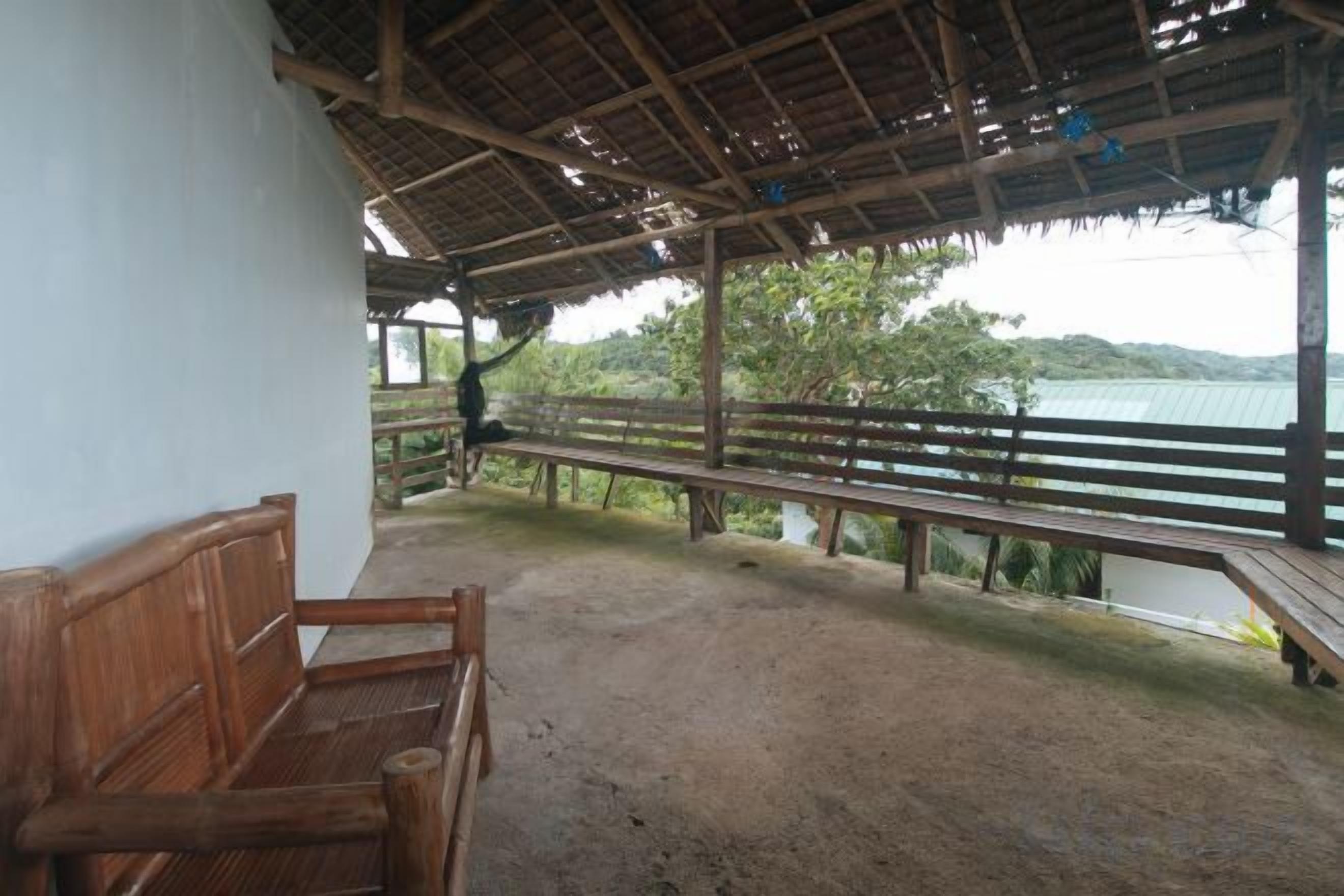 A covered outdoor area with a wooden bench, a railing, and a view of a body of water.