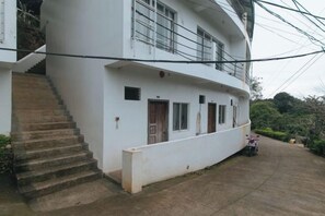 Un bâtiment à deux étages, avec un escalier menant à l’entrée, un espace extérieur couvert et une moto garée.