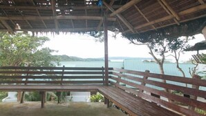 A wooden bench under a thatched roof, overlooking a body of water and greenery. - RedDoorz @ Garvs Boutique Hotel Boracay (Boracay Island)