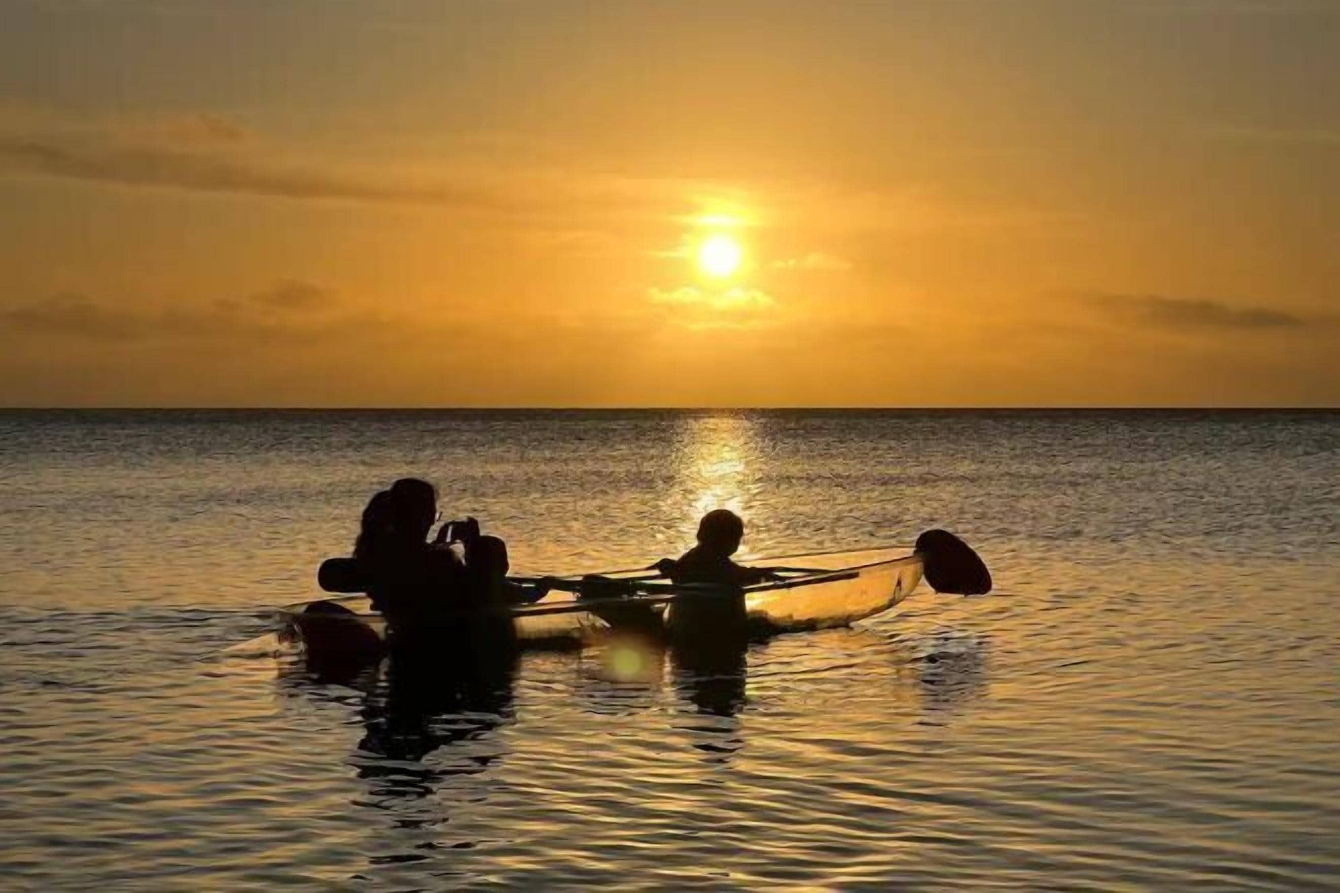 Un coucher de soleil sur une mer calme, avec des personnes qui rament dans un bateau.