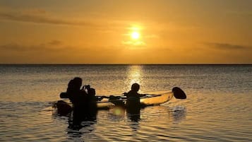 Un coucher de soleil sur une mer calme, avec des personnes qui rament dans un bateau.