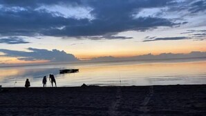 A beach scene with calm water, a pier, and silhouettes of people. - Roseneath Holiday Park (Meerlieu)