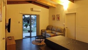 A room with a sofa, a table, a sliding glass door leading to a balcony, and a ceiling with exposed beams. - Roseneath Holiday Park (Meerlieu)