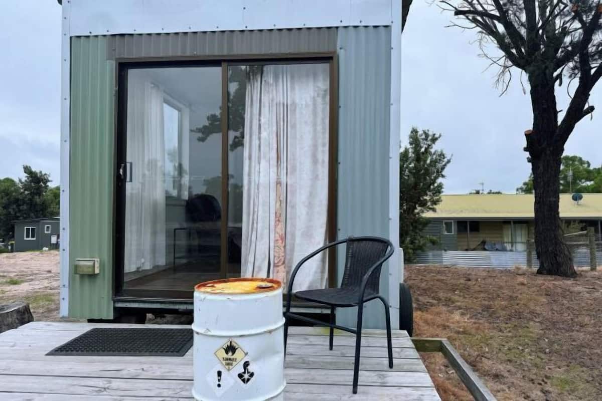 Un pequeño edificio de un piso con puerta de vidrio corredera, una terraza de madera y una silla.