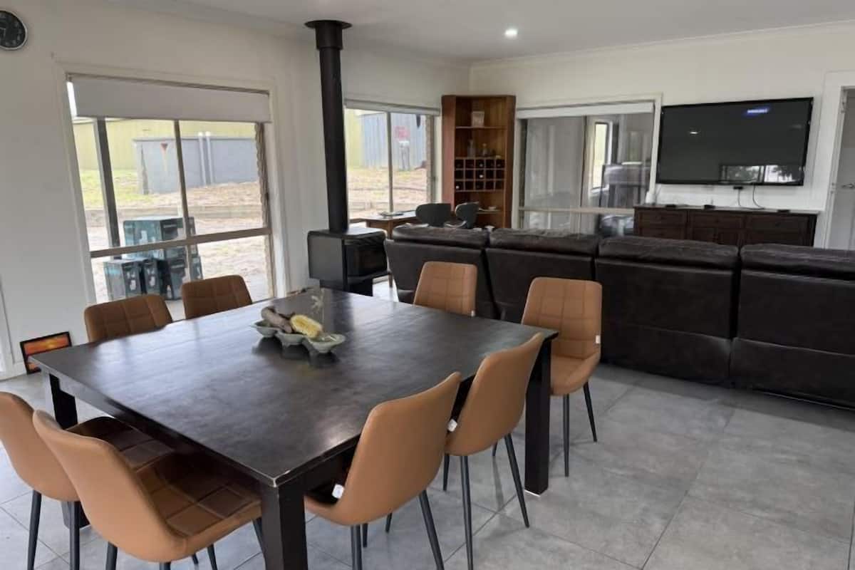 Una sala de estar moderna con una mesa de comedor de madera oscura, sillas color beige, un sofá negro, un televisor y una chimenea.