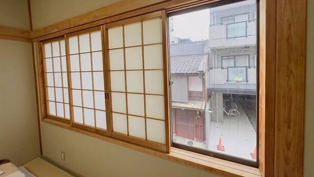 Habitación con un amplio ventanal de biombos shoji, vigas de madera y vistas a edificios.