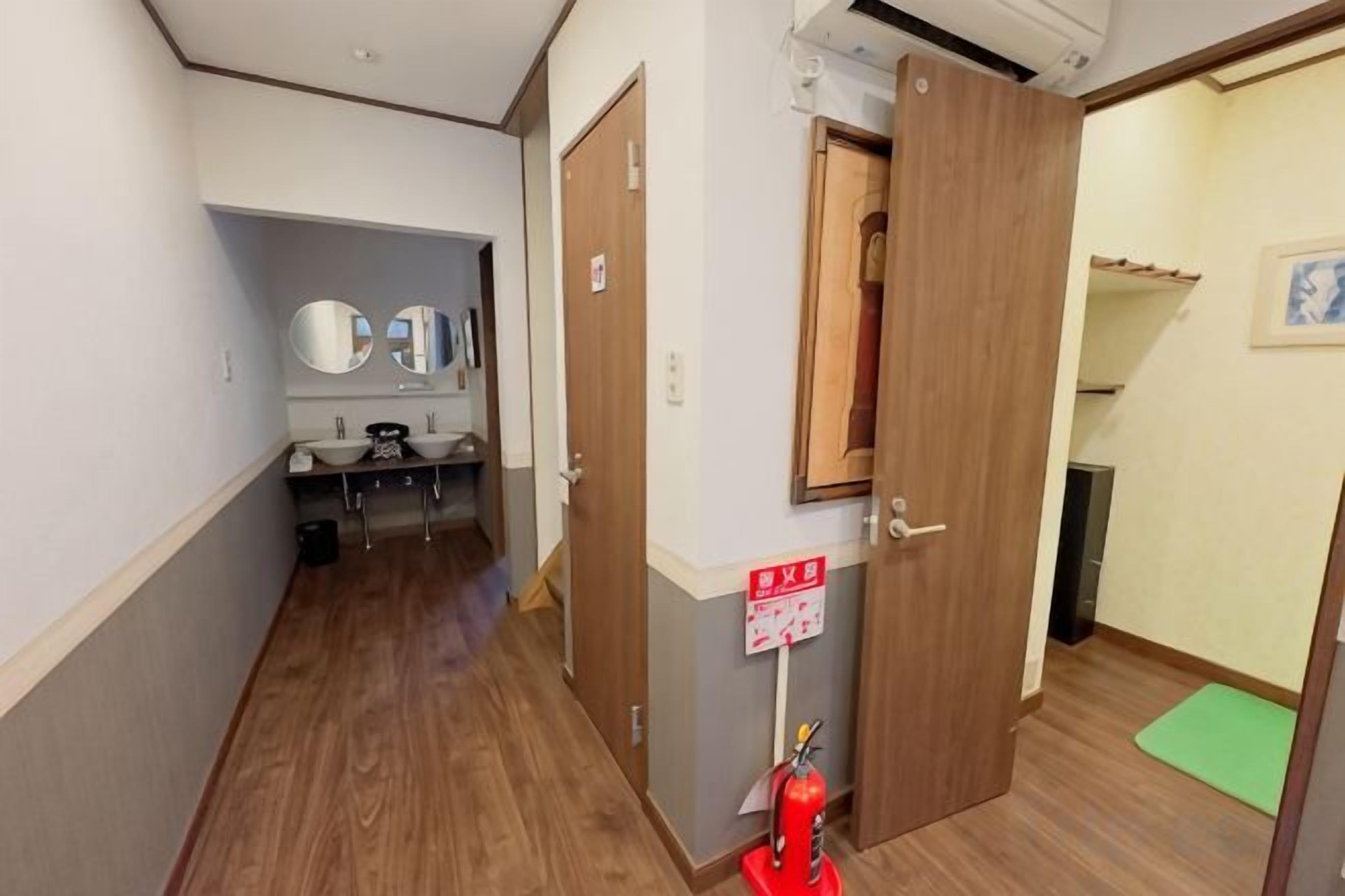 A hallway with a wooden floor, a mirror, a sink, and a fire extinguisher.