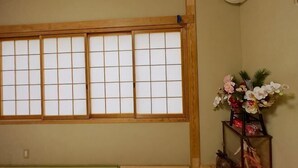 Una habitación con una puerta corredera tradicional, un pequeño estante con flores y un equipo de aire acondicionado.