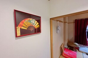 Une pièce avec une œuvre d’art représentant un éventail encadrée au mur, une porte en bois et un lit recouvert d’une couverture rouge.