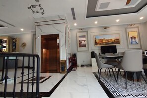 Un vestíbulo de hotel con piso de mármol, una escalera, un comedor con sillas y una mesa, y un televisor.