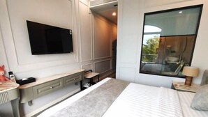 Una habitación de hotel moderna con una cama grande, un escritorio con cajones, un televisor de pantalla plana montado en la pared y un ventanal con vistas al exterior.
