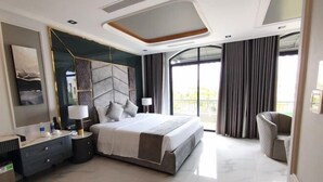 Habitación de hotel moderna con una cama grande, tocador, una silla y un balcón con cortinas.