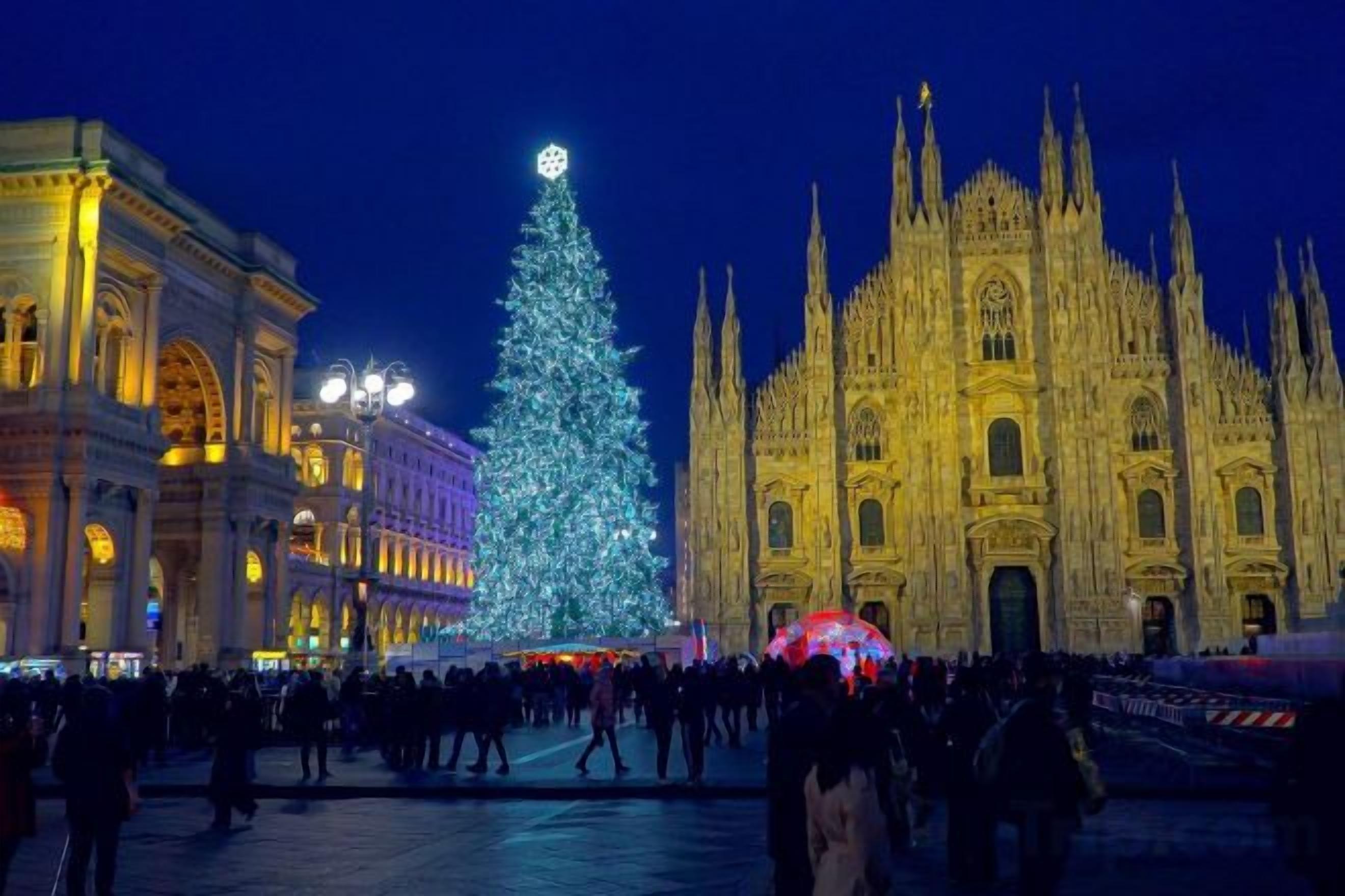 Un gran árbol de Navidad iluminado frente a una catedral histórica, con una multitud de gente.