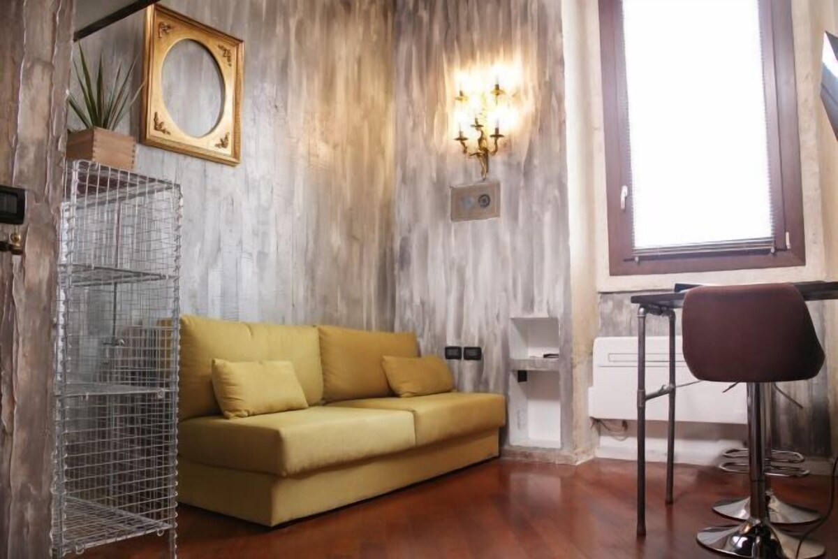 Una stanza con parete in legno, un divano, una mensola in metallo, una sedia e una finestra.