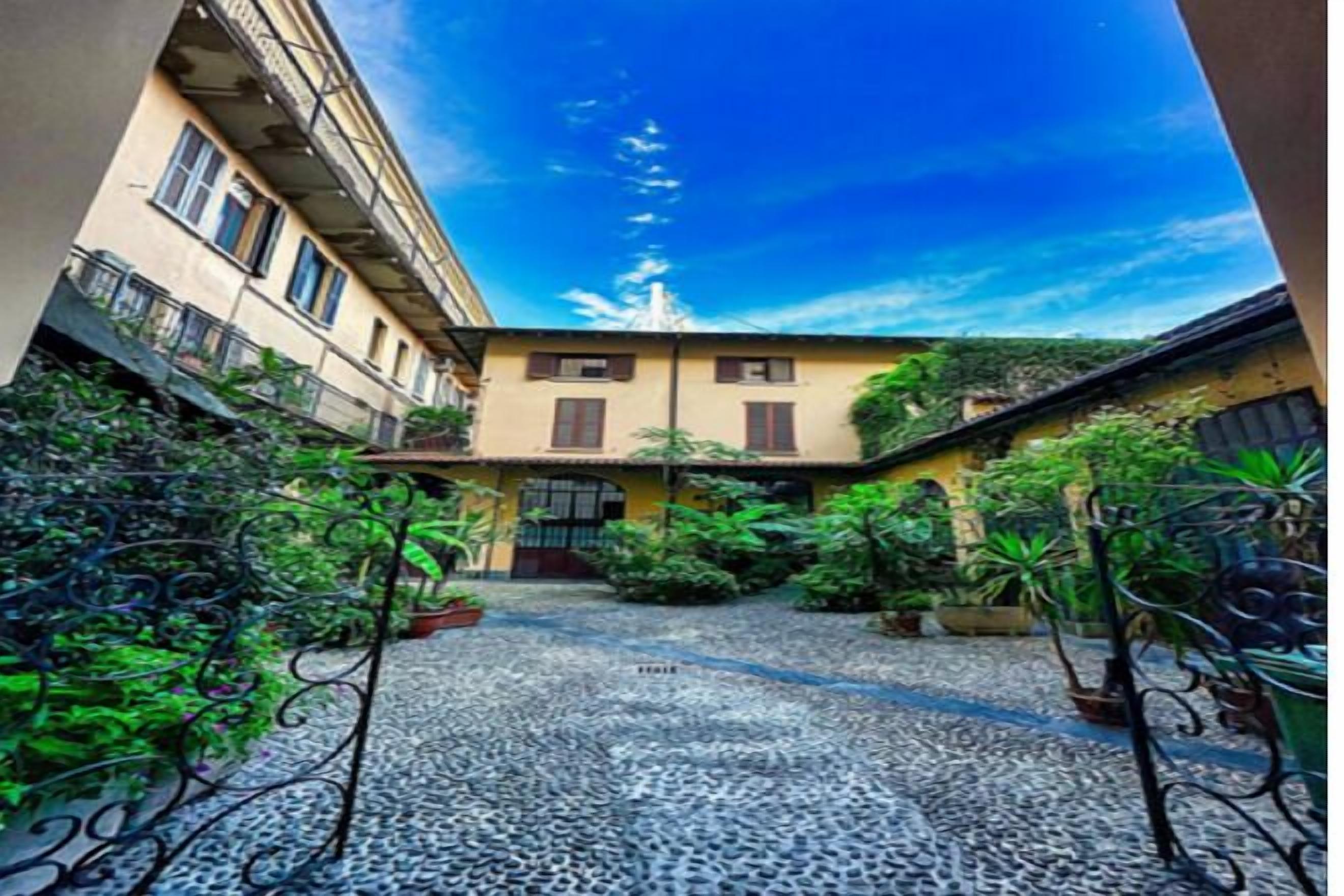 A courtyard with a cobblestone path, potted plants, and a building with a balcony.