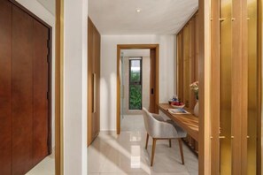 Un couloir avec une porte en bois, un bureau avec une chaise, et une vue sur la verdure à l’extérieur.