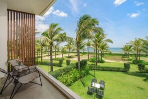 Un balcon avec vue sur une plage, des palmiers et une pelouse bien entretenue.