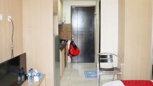 A hotel room with a bed, a TV, a chair, a desk with a computer, and a door leading to a kitchen area. - Taman Sari Sudirman Studio Deluxe B / Near MRT / Central Jakarta (South Jakarta)