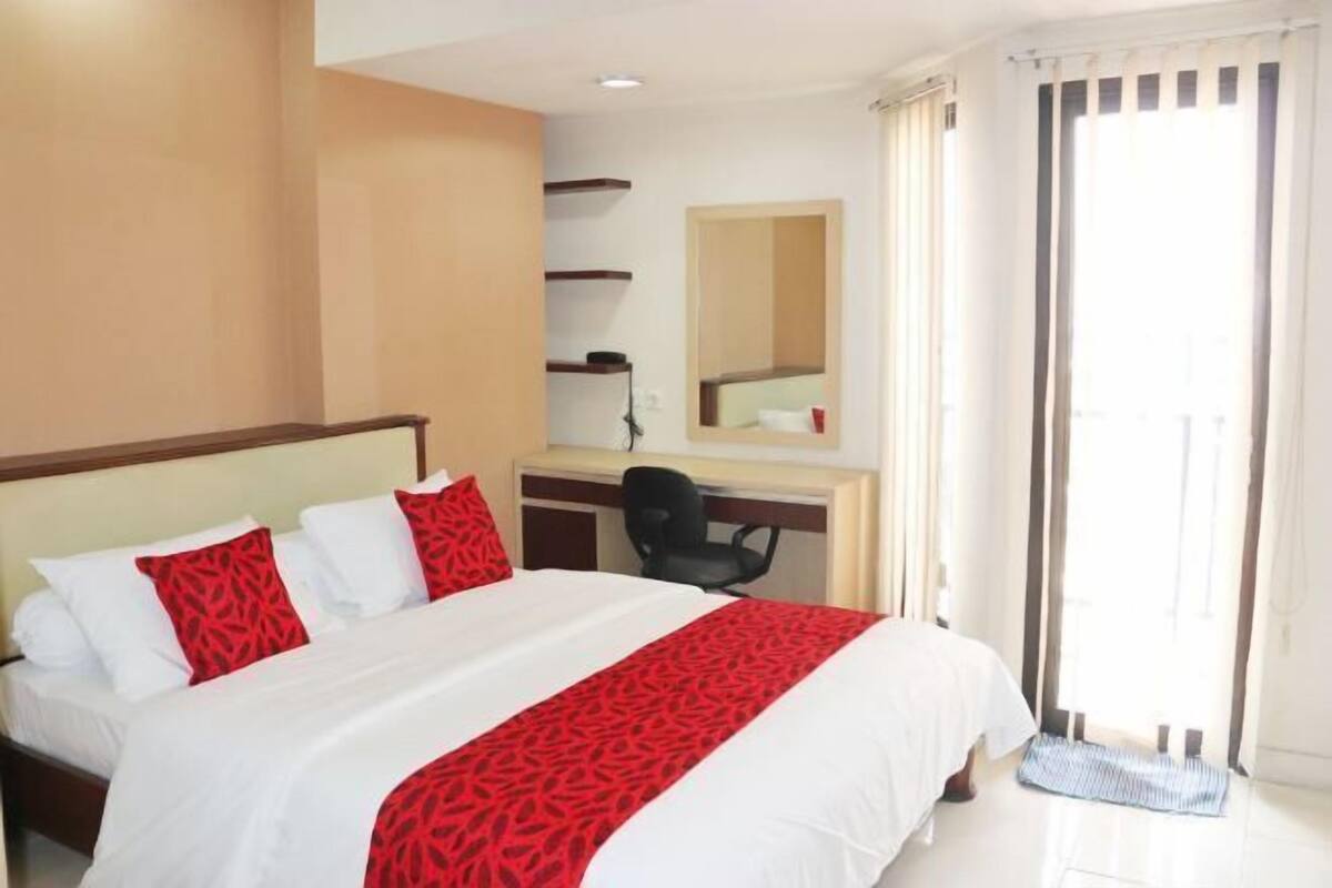 Ein Hotelzimmer mit Bett, Schreibtisch, Stuhl und einem großen Fenster mit Vorhängen.