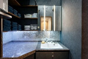 A bathroom with a marble sink, a mirror, shelves with towels, and a tiled backsplash. - Studio House Grand Piano / near JR Shinjuku stn　 (Tokyo)