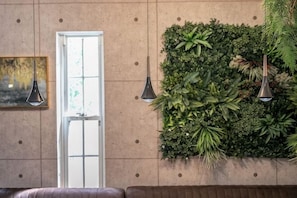 Una habitación con un ventanal amplio, una pared cubierta de plantas y un sofá marrón.