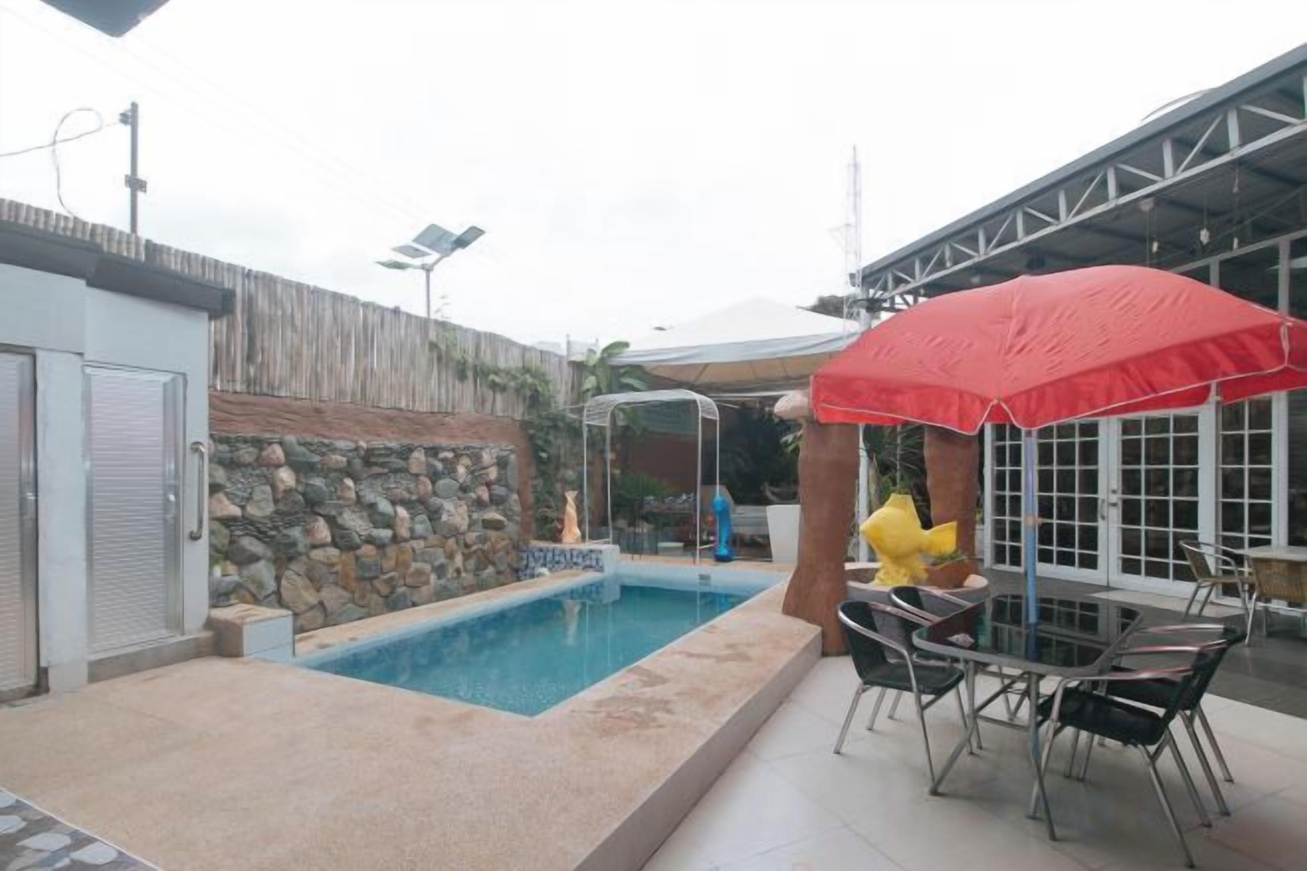 A swimming pool with a covered area, outdoor seating, and a stone wall.