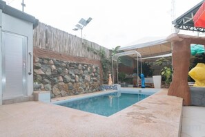 Une piscine avec un mur en pierre et un espace abrité doté d’un auvent.