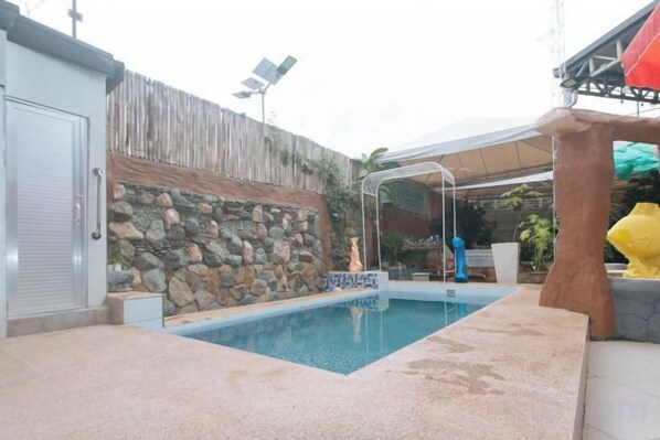 A swimming pool with a stone wall and a covered area with a canopy. - RedDoorz Premium @ Casa LenidaRose (Angeles)