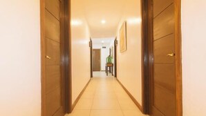 Un pasillo con puertas de madera y suelo de baldosas, que conduce a una habitación con una silla y una mesa.