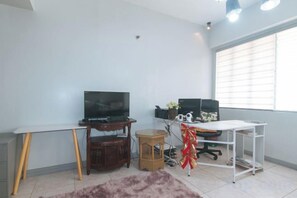 A room with a white desk, a television, and a window with blinds. - Winland JY7 Cebu by RedDoorz (Cebu City)