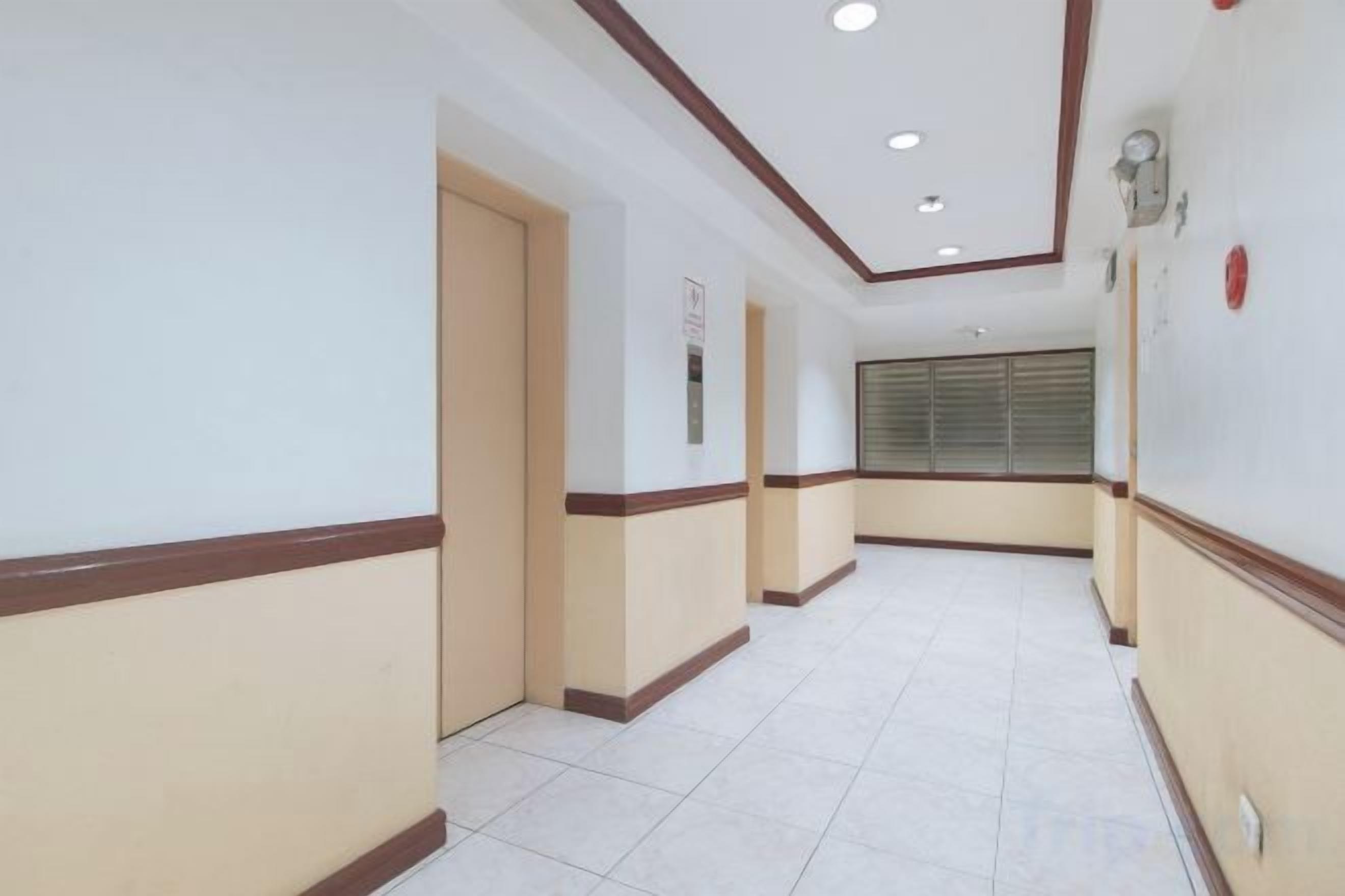 A hallway with doors, a window with blinds, and a light fixture on the wall.