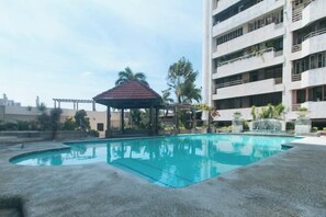 Une piscine avec un kiosque, un immeuble à plusieurs étages et un ciel dégagé.