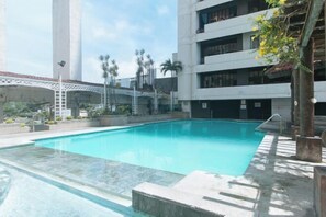 A swimming pool with a clear blue water, surrounded by a concrete deck and a white building with balconies. - Winland JY7 Cebu by RedDoorz (Cebu City)