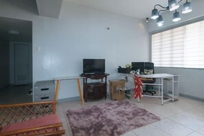 A living room with a television, a desk, and a computer. There is a window with blinds, a door, and a purple rug. - Winland JY7 Cebu by RedDoorz (Cebu City)