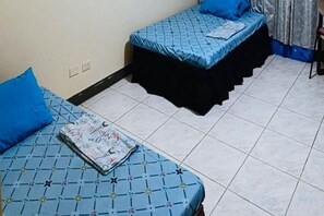Una habitación con dos camas, cada una con colcha azul y patas cubiertas por una falda negra.