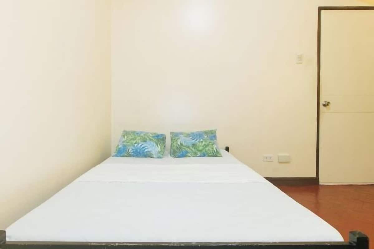 A simple room with a bed, two pillows, a door, and a light switch on the wall.