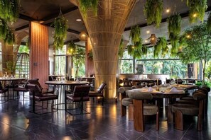 Un restaurant avec de hauts plafonds, des plantes suspendues et différents types d’aménagements pour les places assises.