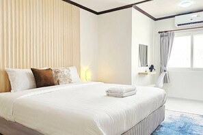 A hotel room with a large bed, a bedside table, a window with curtains, and an air conditioning unit. - Greta Villa (Pattaya)