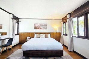 A hotel room with a large bed, a desk, and a window with curtains. - Greta Villa (Pattaya)
