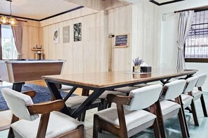 A dining area with a wooden table and chairs, a reception desk, and a view through a window. - Greta Villa (Pattaya)