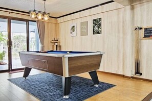 A pool table in a room with wooden flooring and a blue rug. - Greta Villa (Pattaya)