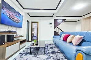 A modern living room with a blue sofa, a flat-screen TV mounted on the wall, and a coffee table. - Greta Villa (Pattaya)