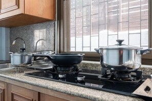 A kitchen with a gas stove, pots, and a window with blinds. - Greta Villa (Pattaya)