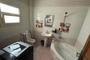 A bathroom with a toilet, sink, bathtub, and a window. - Orange Chinese Hotel (New Cairo City)