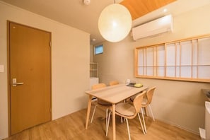 A room with a wooden dining table, wicker chairs, a large window with a view, and a ceiling light fixture. - FOXINN (Osaka)